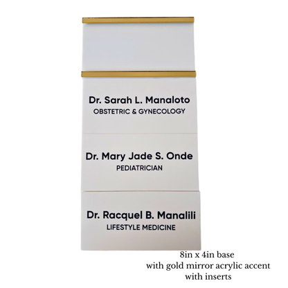 Three white personalized wall sign base and room sign inserts stacked vertically, each with a gold mirror horizontal accent bar on the top & bottom of the room sign base. The room inserts are printed with black text showing different doctor names.